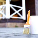White paint and paint brush. Painted home terrace on the background.