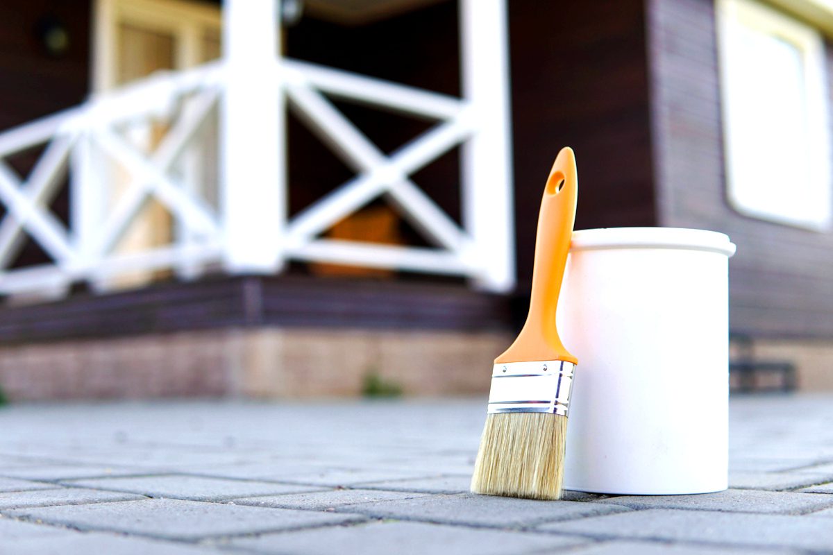 White paint and paint brush. Painted home terrace on the background.