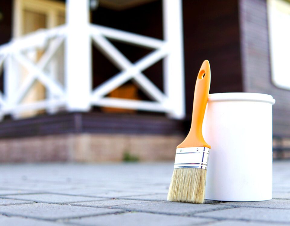 White paint and paint brush. Painted home terrace on the background.